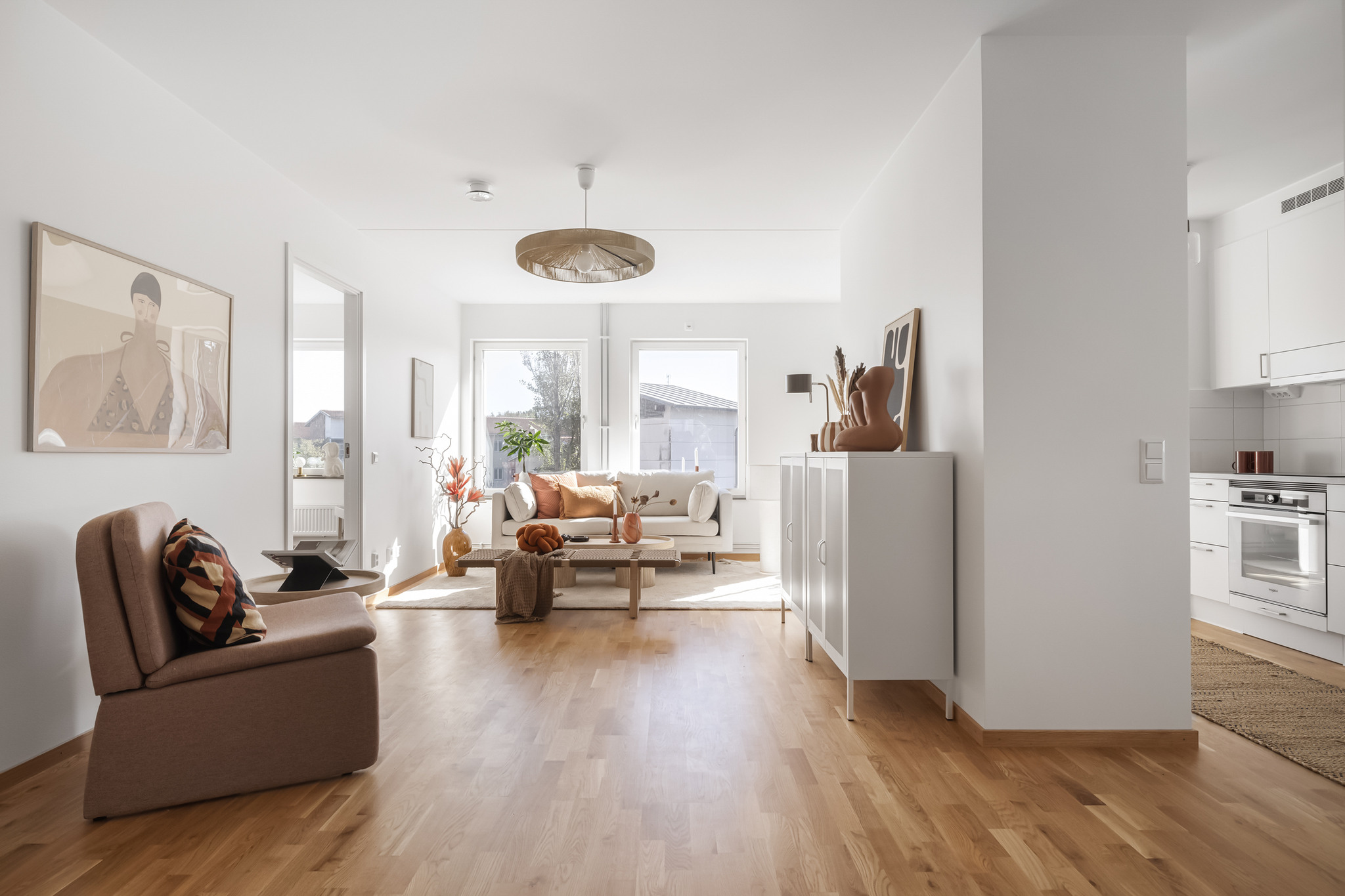 Vardagsrum med öppen planlösning. Inredd med en soffa, fåtölj, byrå och trägolv i trestavig ekparkett.